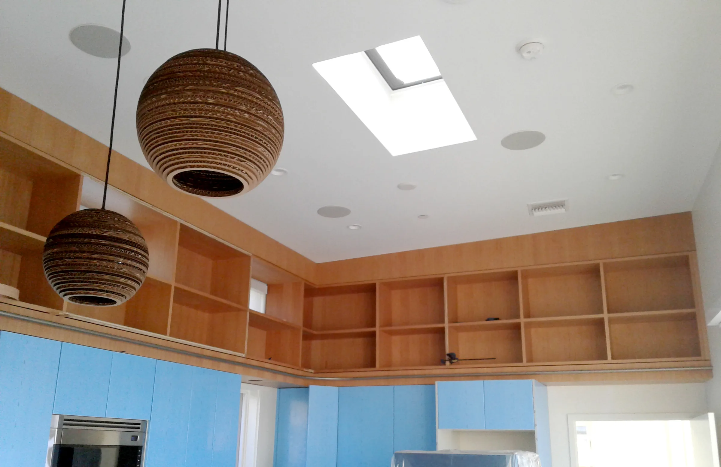 Fir shelving running around a kitchen ceiling above blue cabinets, with paper pendant lamps — furniture and millwork designed and built by Jack Rusk (Oakland and Los Angeles, 2013–2018)