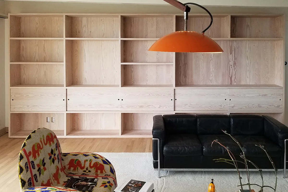 Wall of pale fir shelving and sliding cabinet doors behind a black leather sofa — furniture and millwork designed and built by Jack Rusk (Oakland and Los Angeles, 2013–2018)