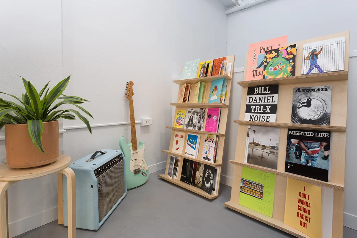 Plywood display racks holding zines and records beside a guitar and amplifier in a white shop — furniture and millwork designed and built by Jack Rusk (Oakland and Los Angeles, 2013–2018)