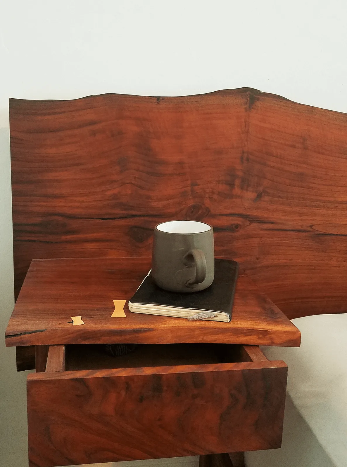 Live-edge walnut bedside table with a drawer and bowtie inlays, holding a mug and notebook — furniture and millwork designed and built by Jack Rusk (Oakland and Los Angeles, 2013–2018)