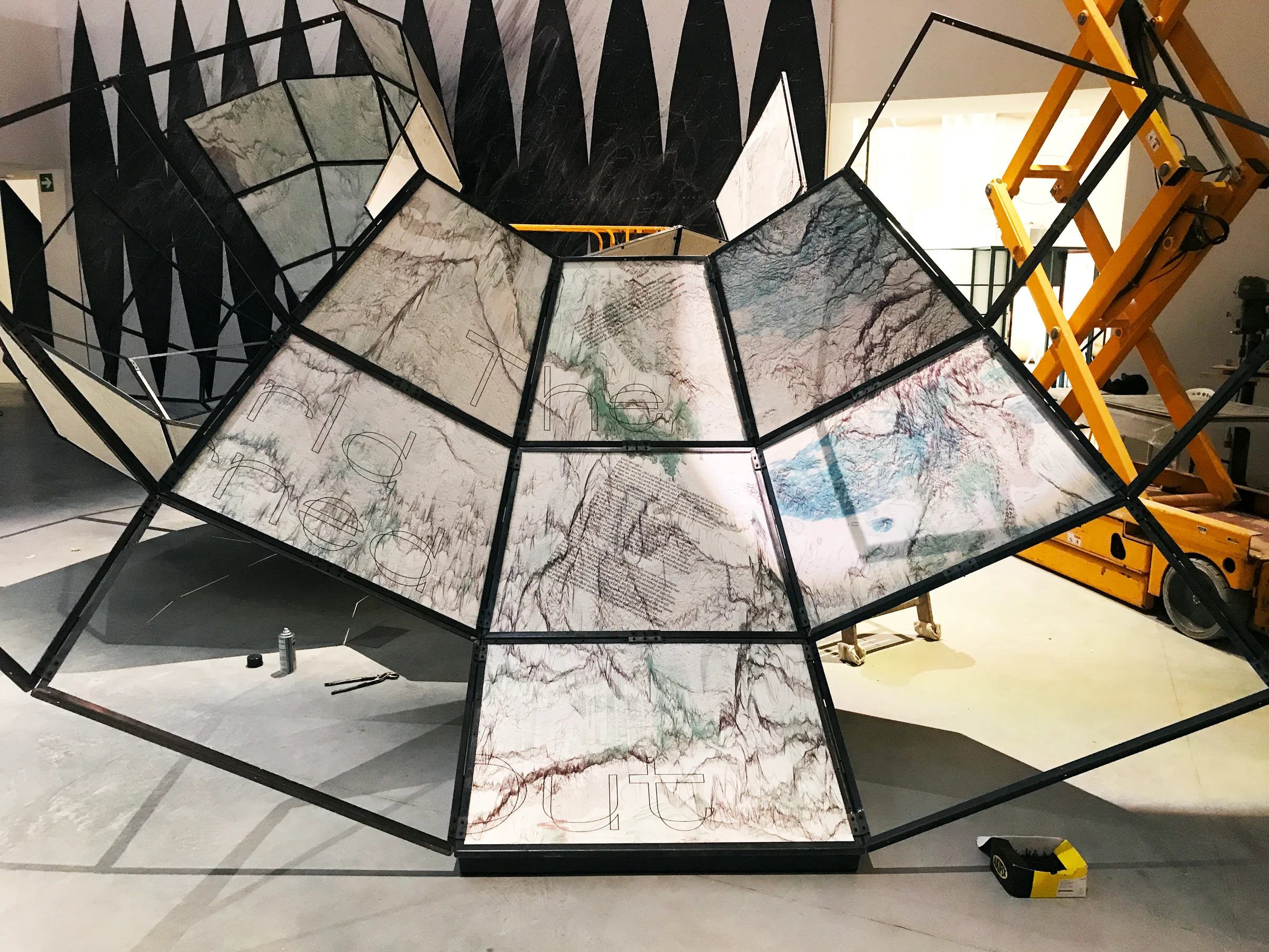 Installation in progress: faceted map panels mounted in a black steel frame, with a scissor lift behind — 'The World Turned Inside Out', fabricated by Jack Rusk with Adare Brown, Christopher Cambio and Tyler Krebs for the 2021 Venice Biennale
