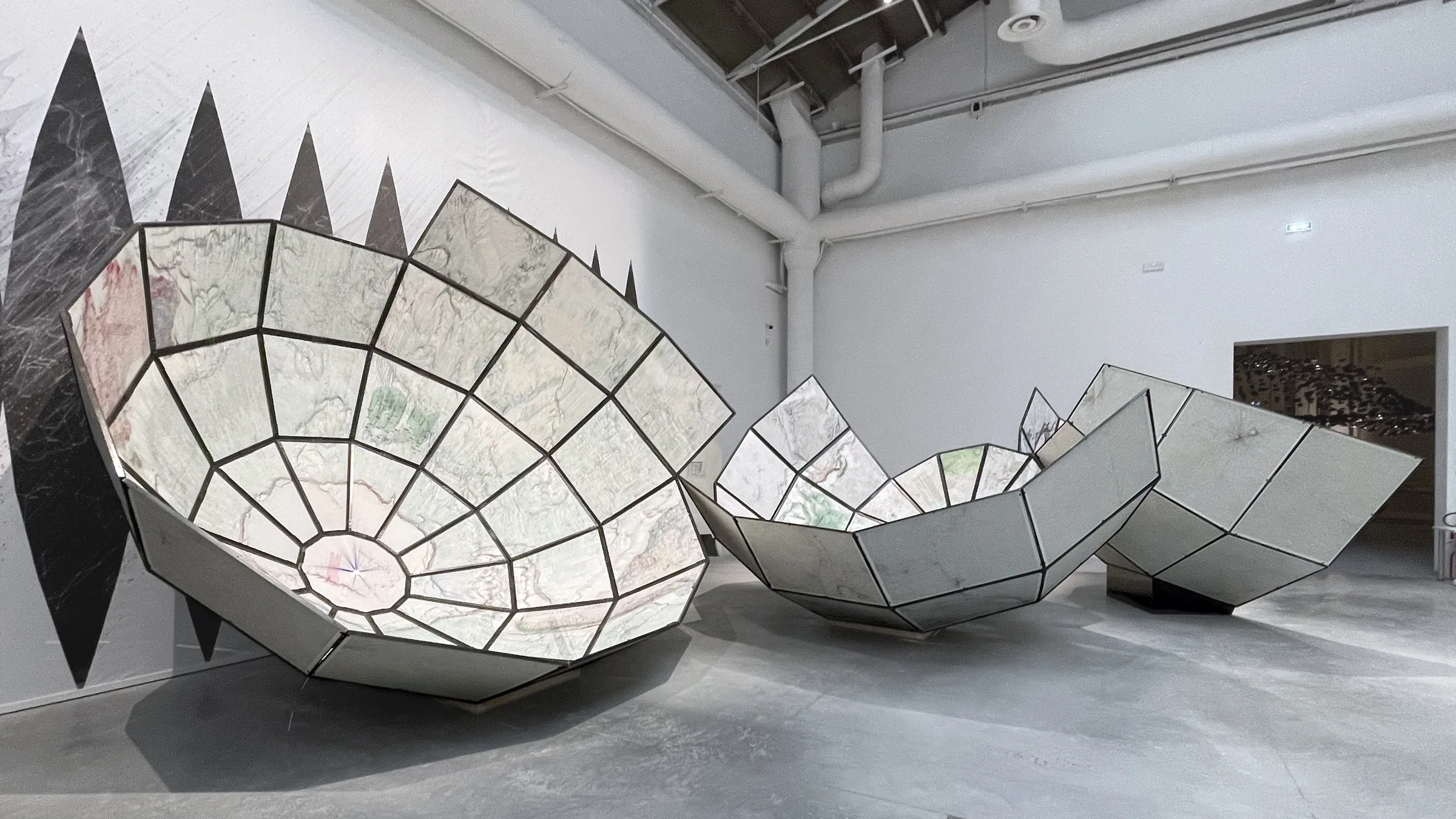 Three large faceted bowl-shaped structures clad in translucent map panels in a white gallery — 'The World Turned Inside Out' by Plan B Architecture & Urbanism at the 2021 Venice Biennale, fabricated by Jack Rusk with Adare Brown, Christopher Cambio and Tyler Krebs